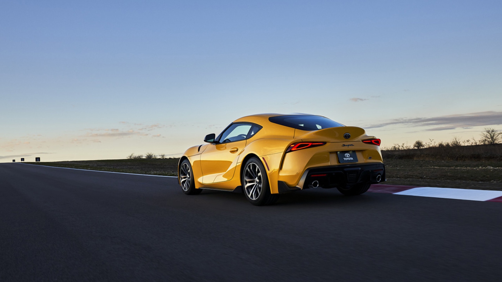 Желтый автомобиль Toyota GR Supra, 2021 года на трассе вид сзади