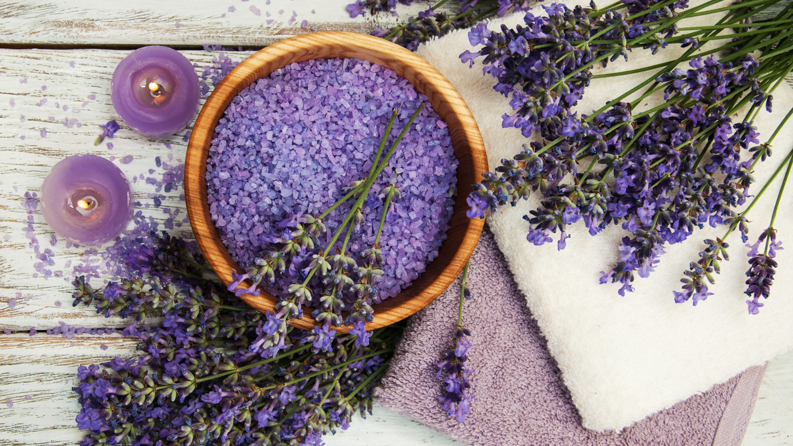 Ароматная соль, на столе с полотенцами, лавандой и зажженными свечами