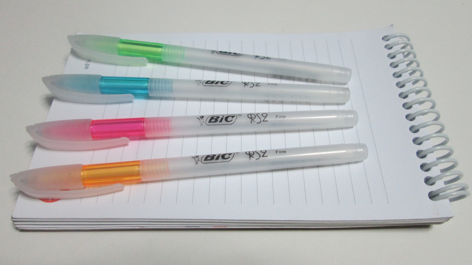 Разноцветные ручки лежат на блокноте на белом фоне 