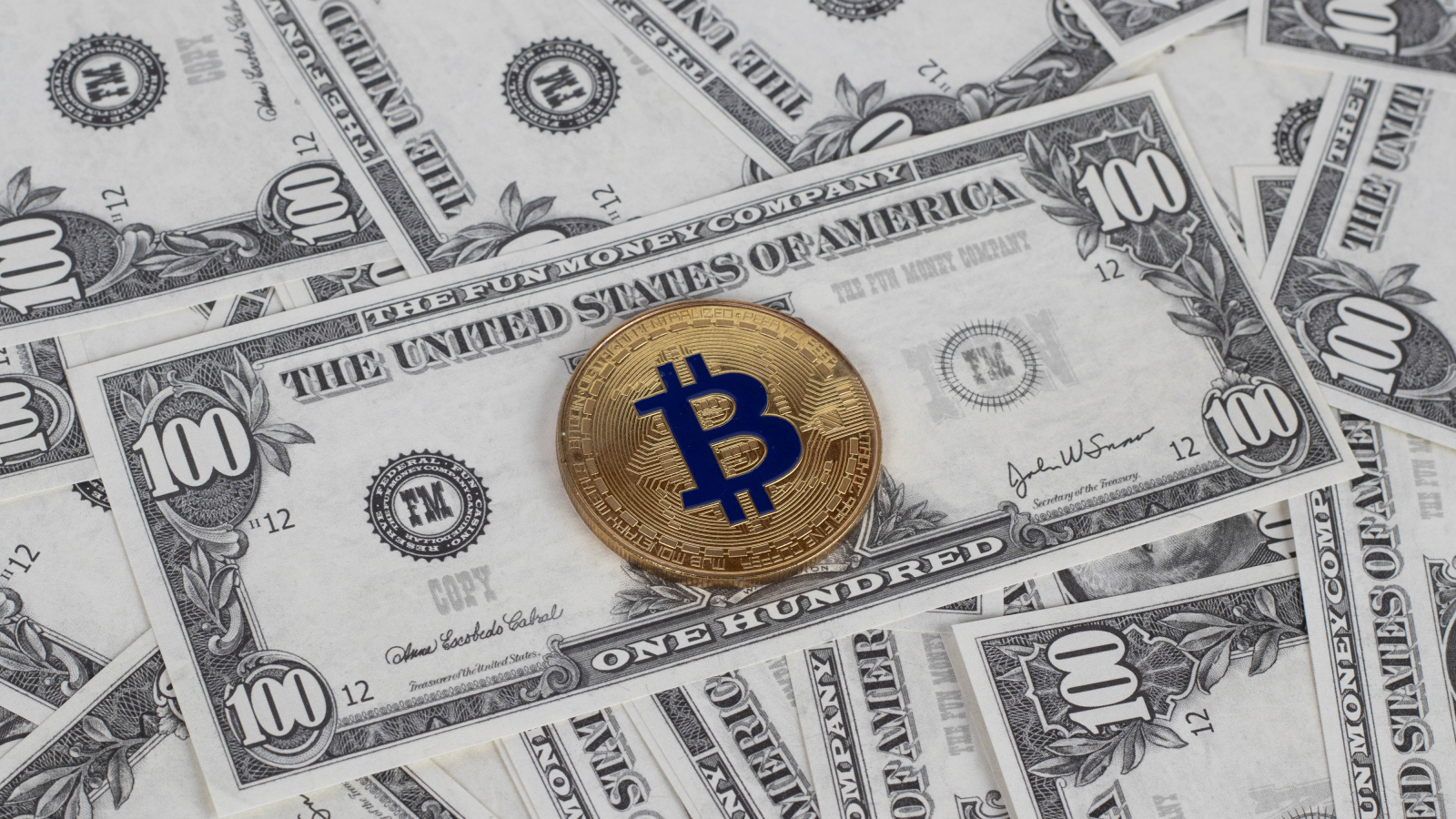 Монета Биткоин лежит на стодолларовых купюрах