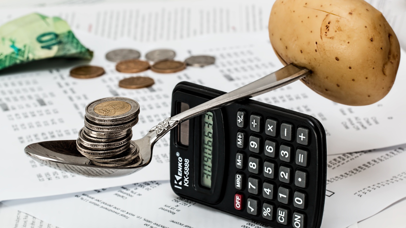 Весы из калькулятора и ложки с монетами и картофелем