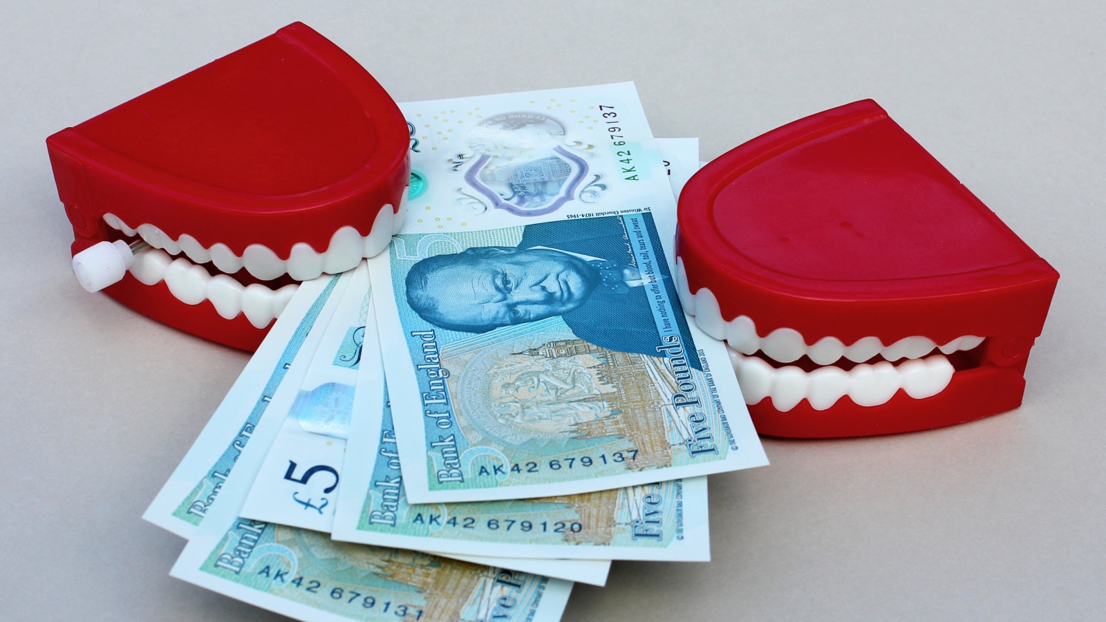 Два держателя денег в форме челюсти с купюрами на сером фоне