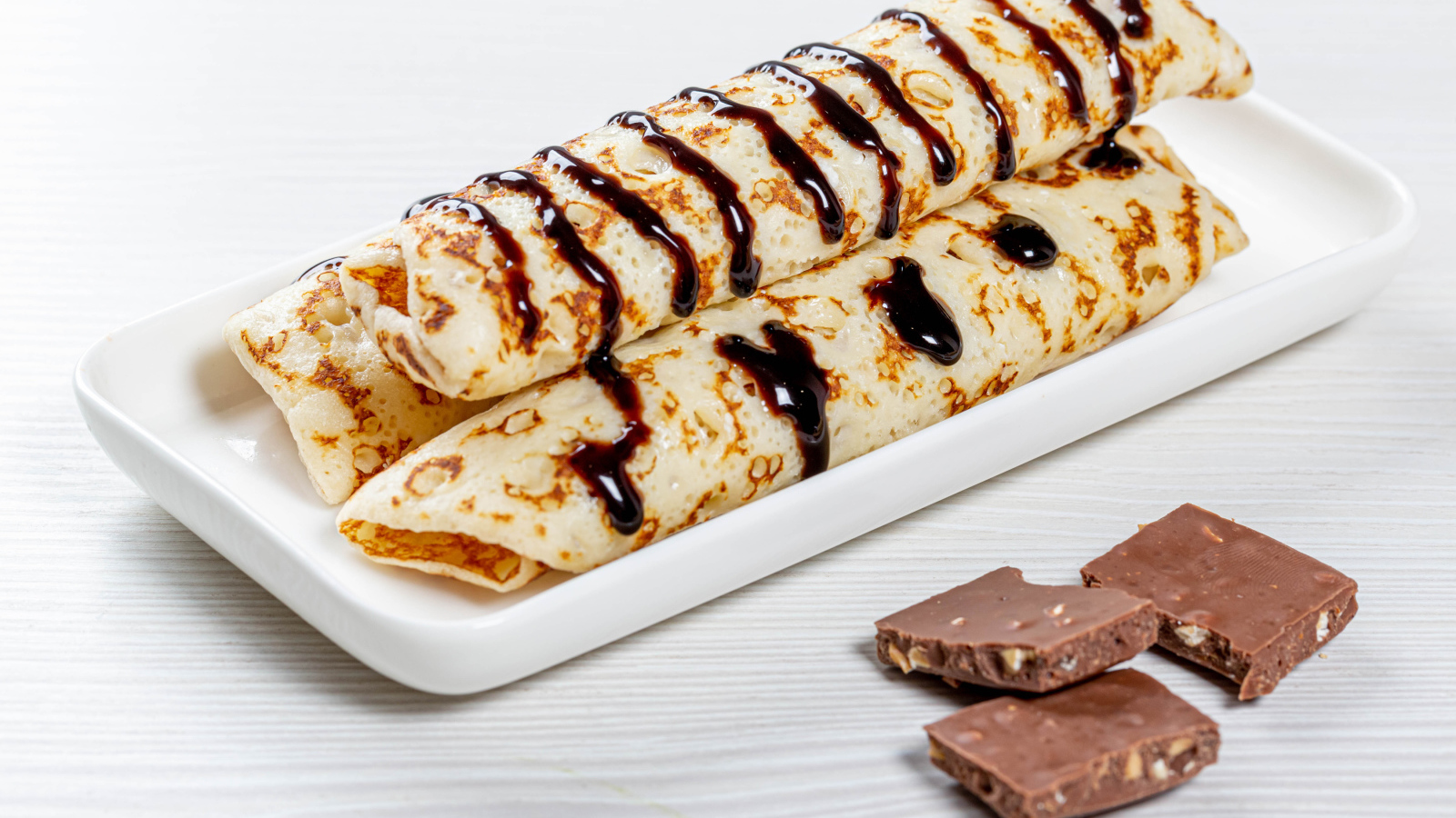 Аппетитные тонкие блины на белой тарелке с шоколадом