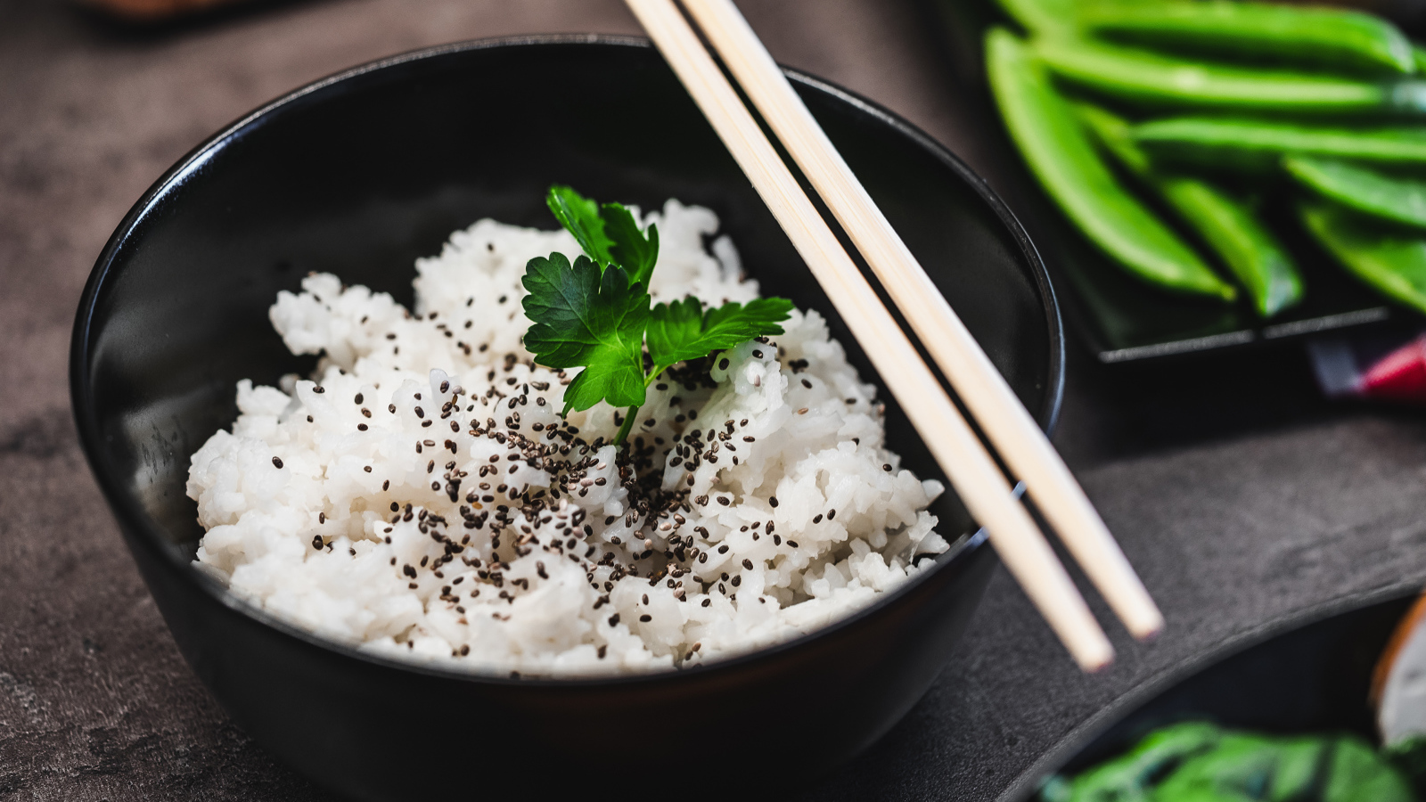 Вареный рис с семенами  в черной миске с палочками