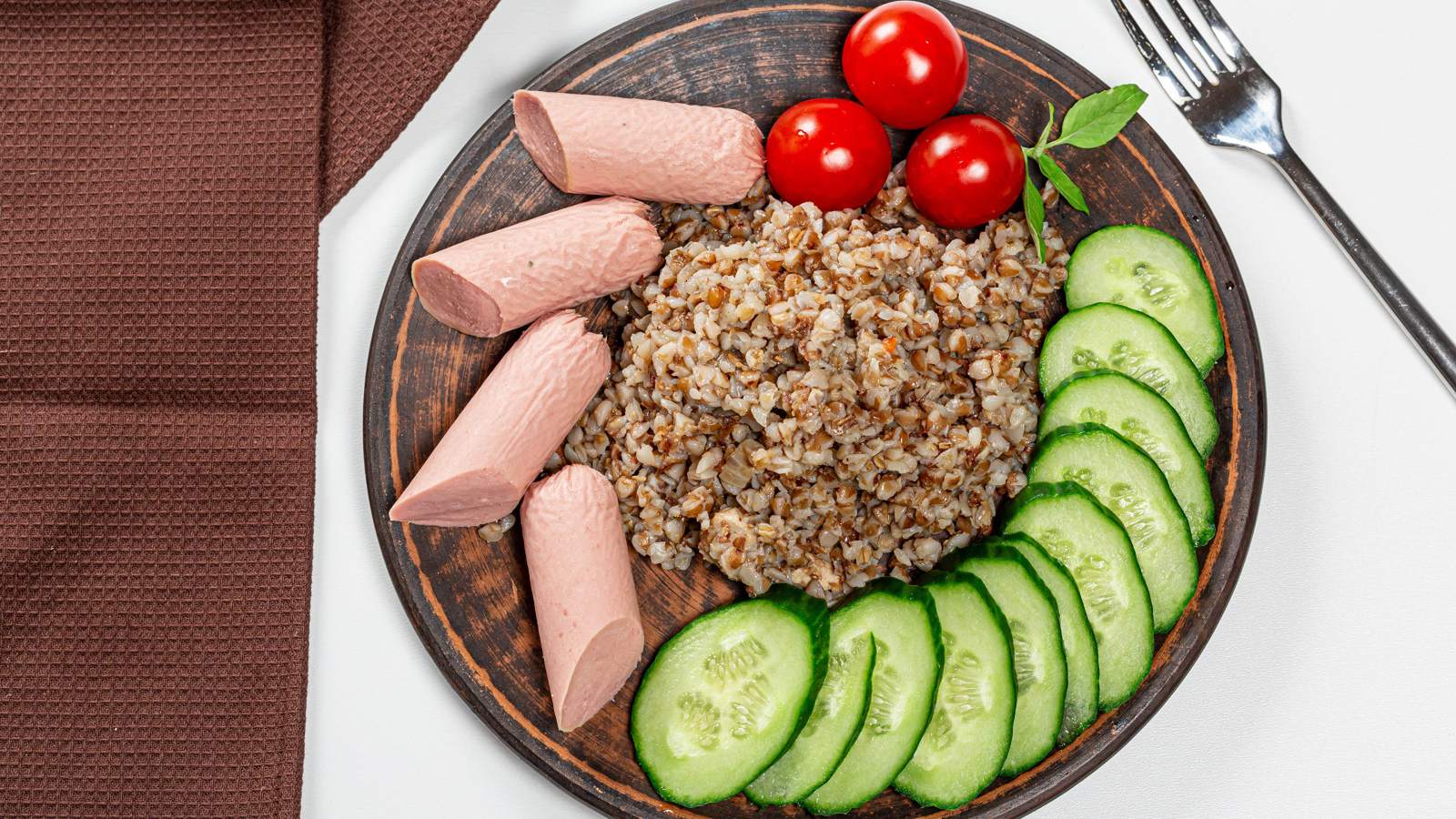 Гречка на тарелке с помидорами, огурцами и сосисками