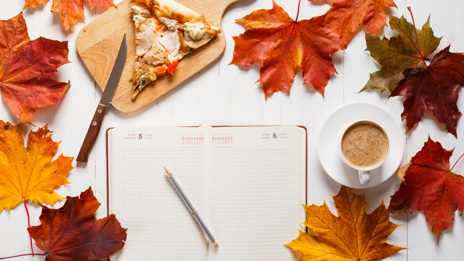 Ежедневник на столе с желтыми листьями, кофе и пиццей 