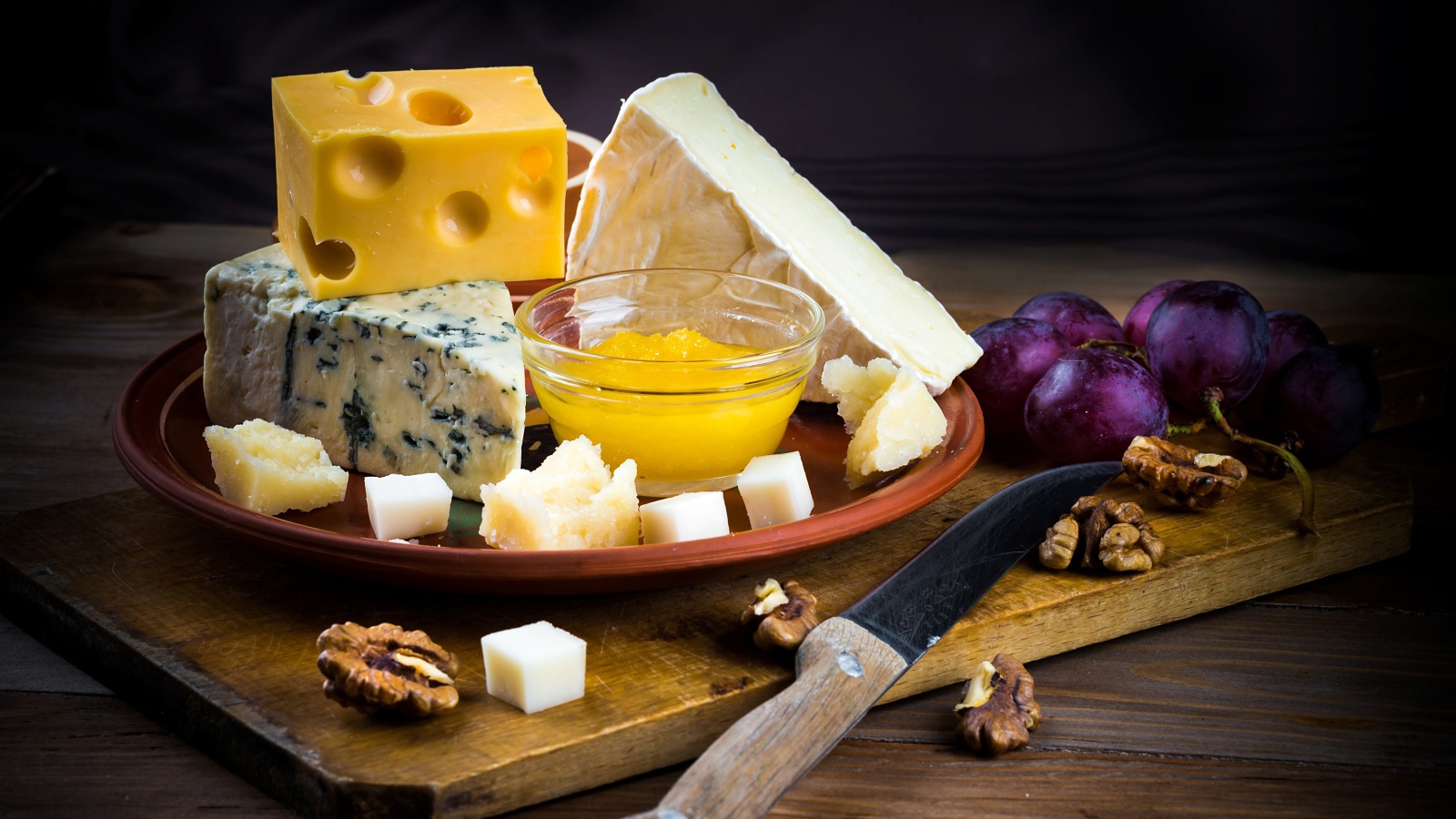 Разные виды сыра на столе с виноградом и орехами