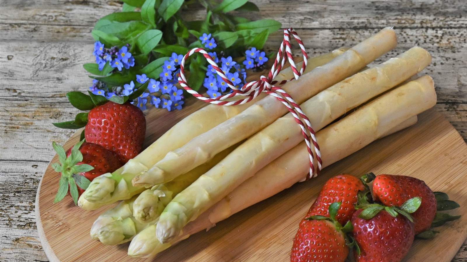 Свежая спаржа на столе с клубникой и цветами незабудками