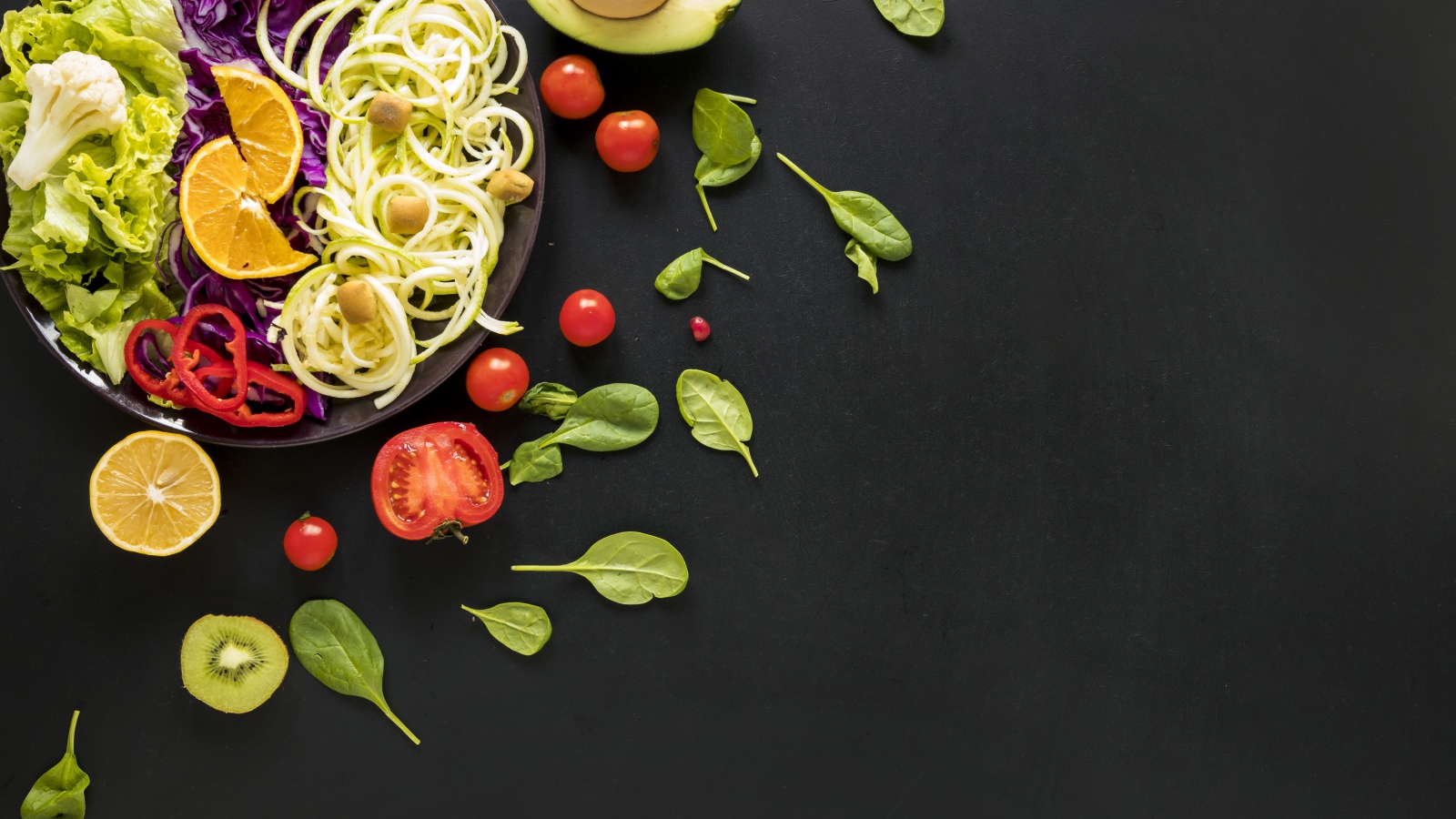 Салат из свежих овощей на черном столе с базиликом, помидорами и авокадо 