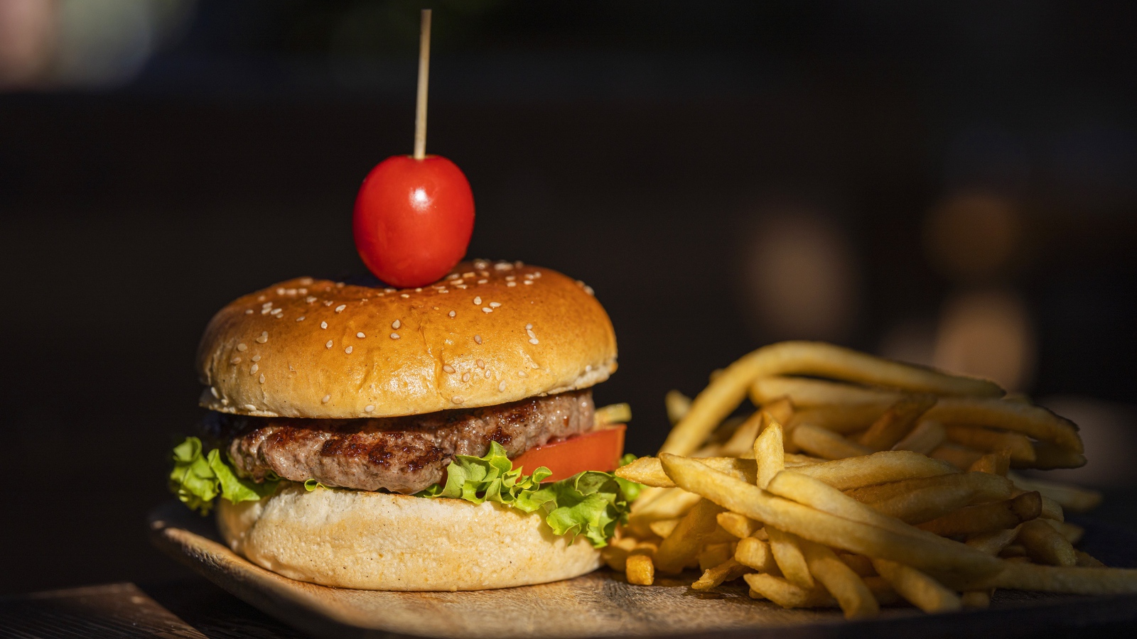 Гамбургер с помидором на доске с картофелем фри 