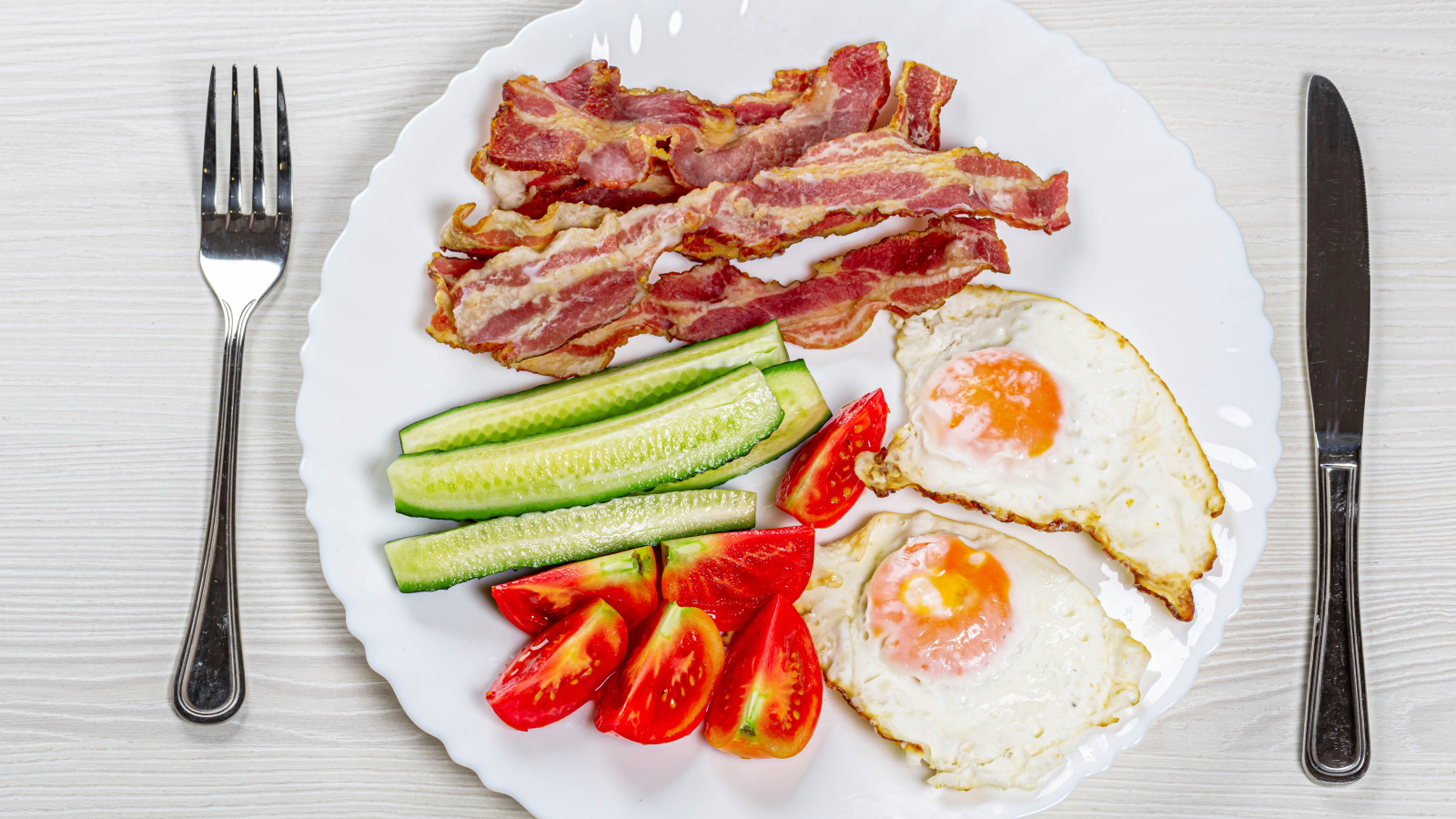 Большая белая тарелка с беконом, огурцами, помидорами и яичницей 