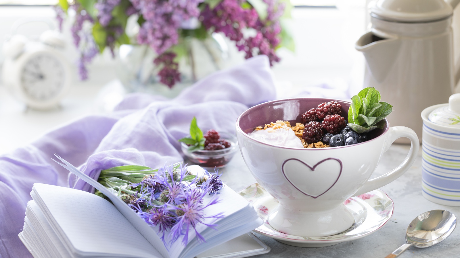 Мюсли с ягодами в чашке на столе с блокнотом и букетом сирени 