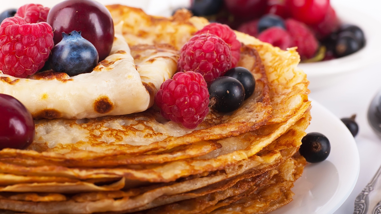 Блины с ягодами черники и малины на белой тарелке 