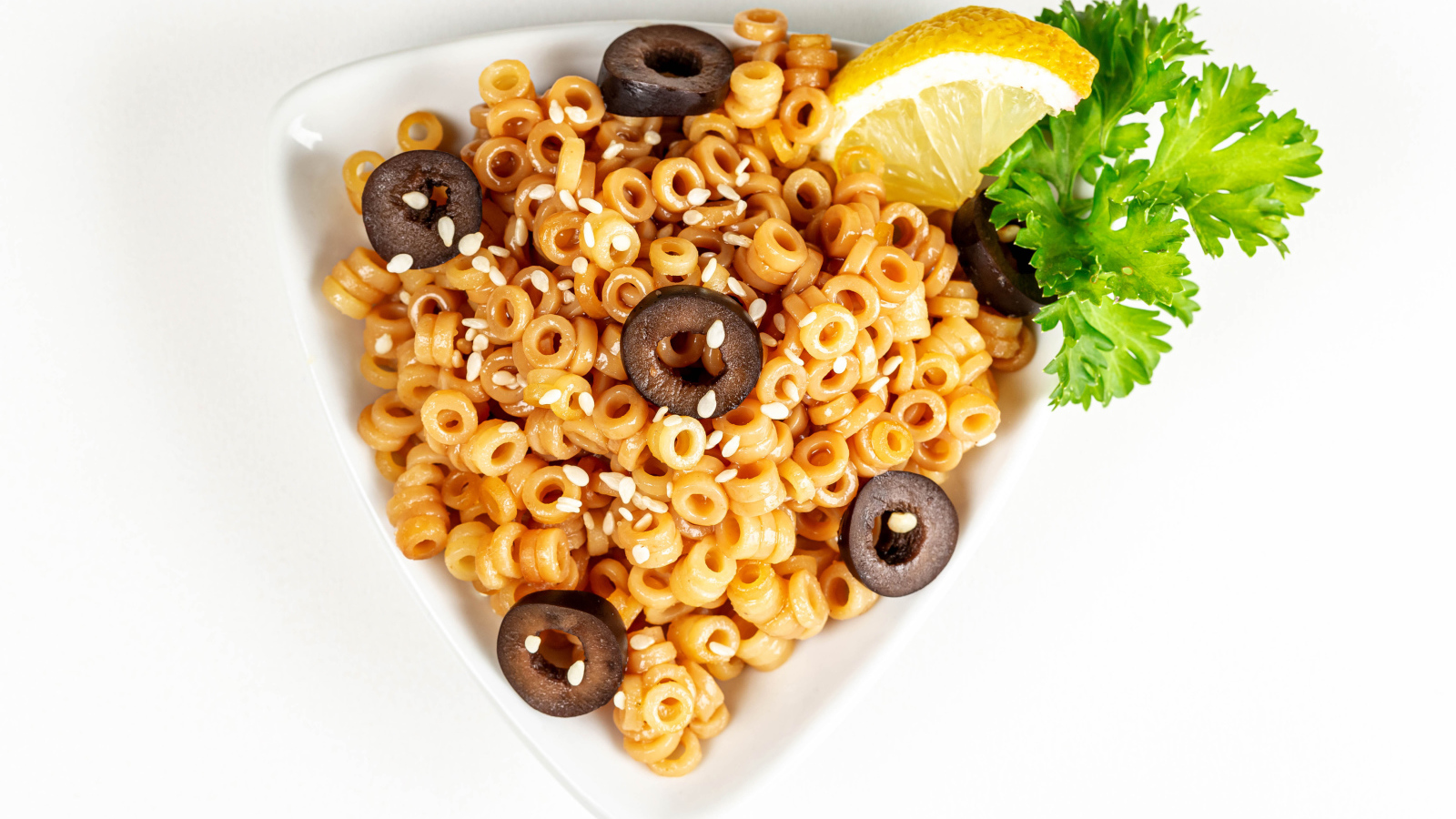 Макароны на тарелке с оливками и лимоном