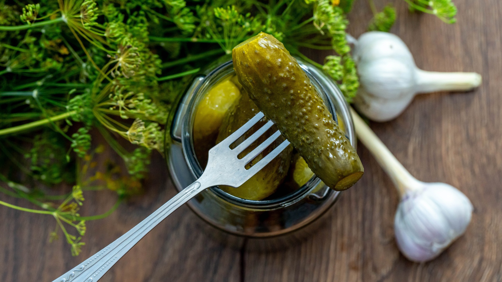 Маринованные огурцы в банке на столе с чесноком и укропом