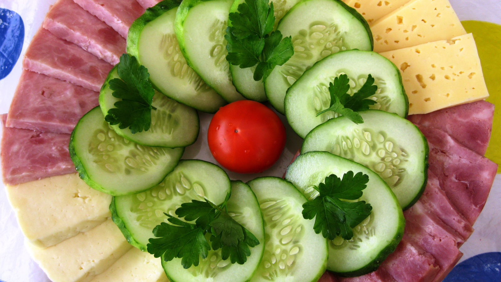 Сыр нарезанный, огурцы и ветчина на тарелке 