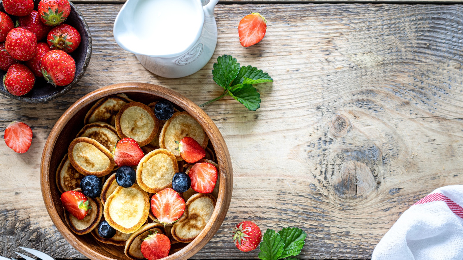 Маленькие оладьи в миске с клубникой и черникой на столе с молоком 