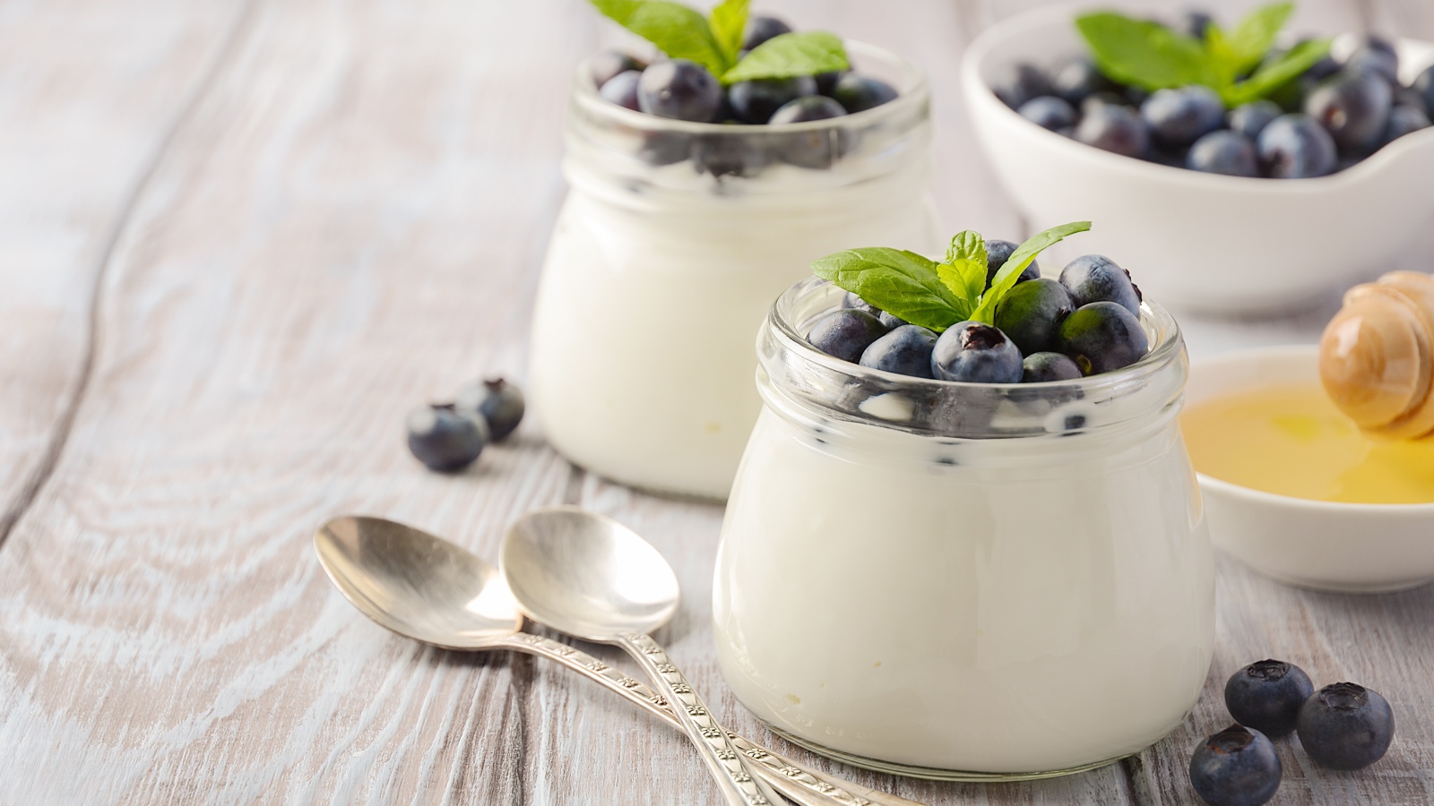 Йогурт в банках с ягодами черники на столе с ложками и медом