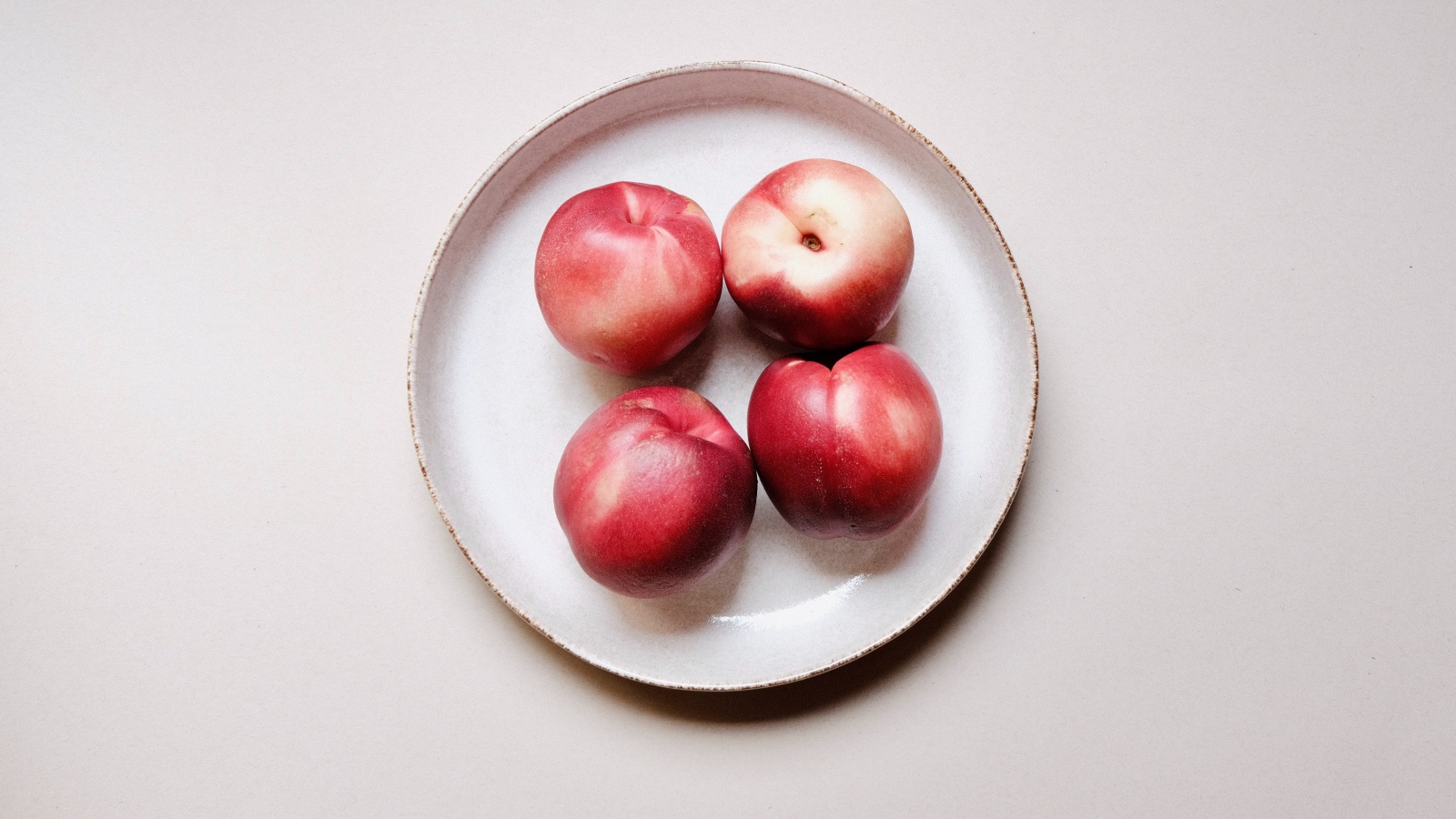 Четыре красных спелых нектарина на тарелке 