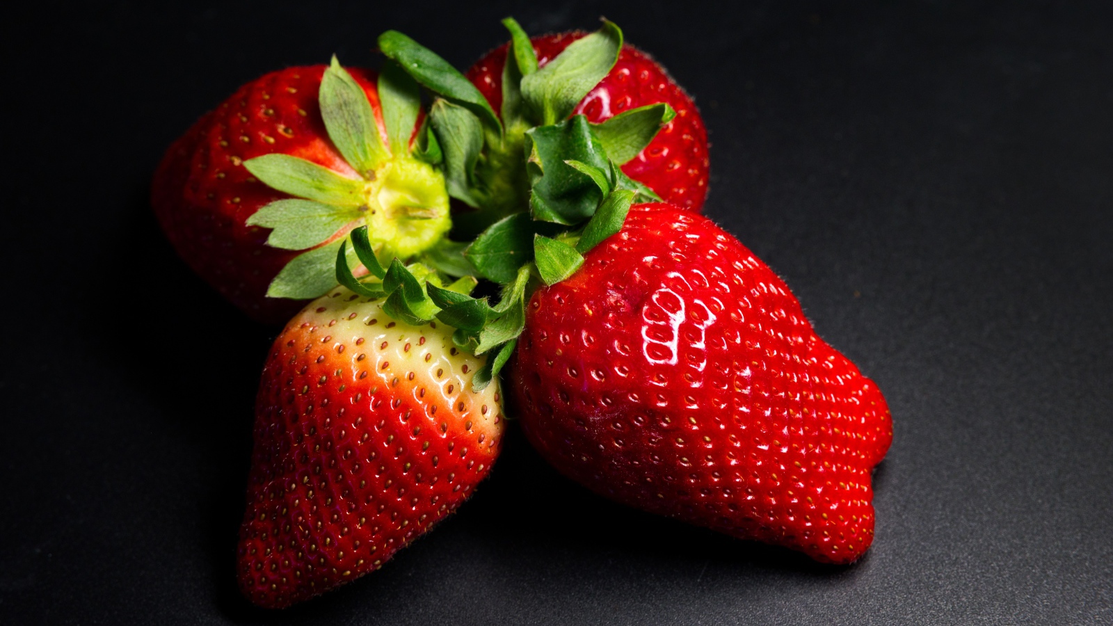 Четыре спелых красных ягоды клубники на черном столе 
