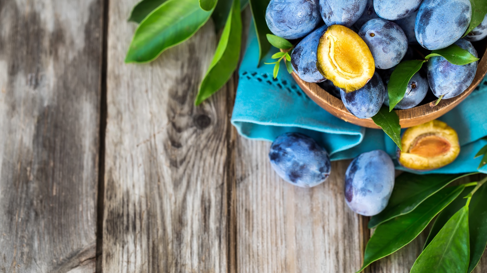 Свежие синие сливы с зелеными листьями на столе 