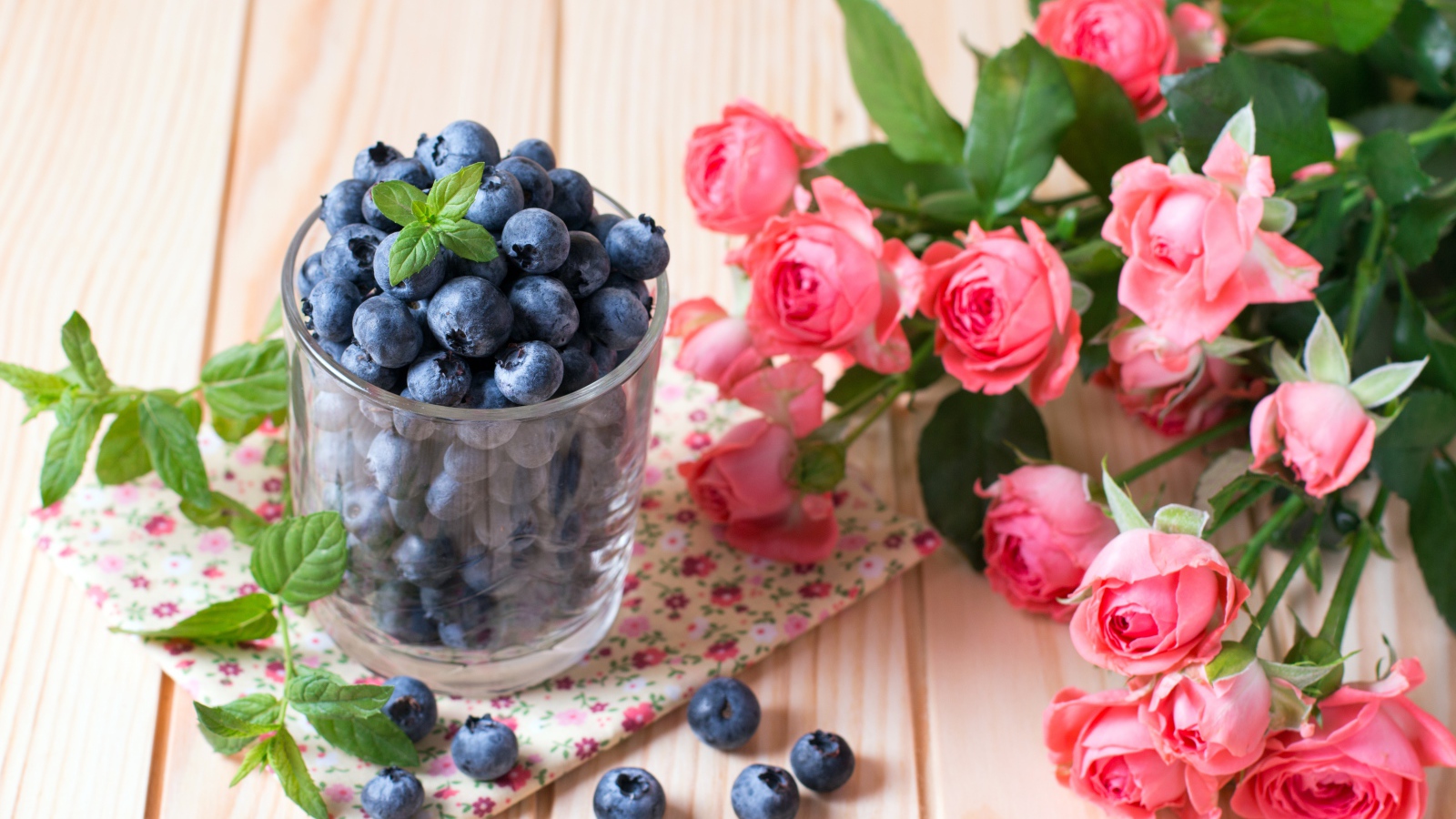 Glass of blueberries on the table with a bouquet of pink roses