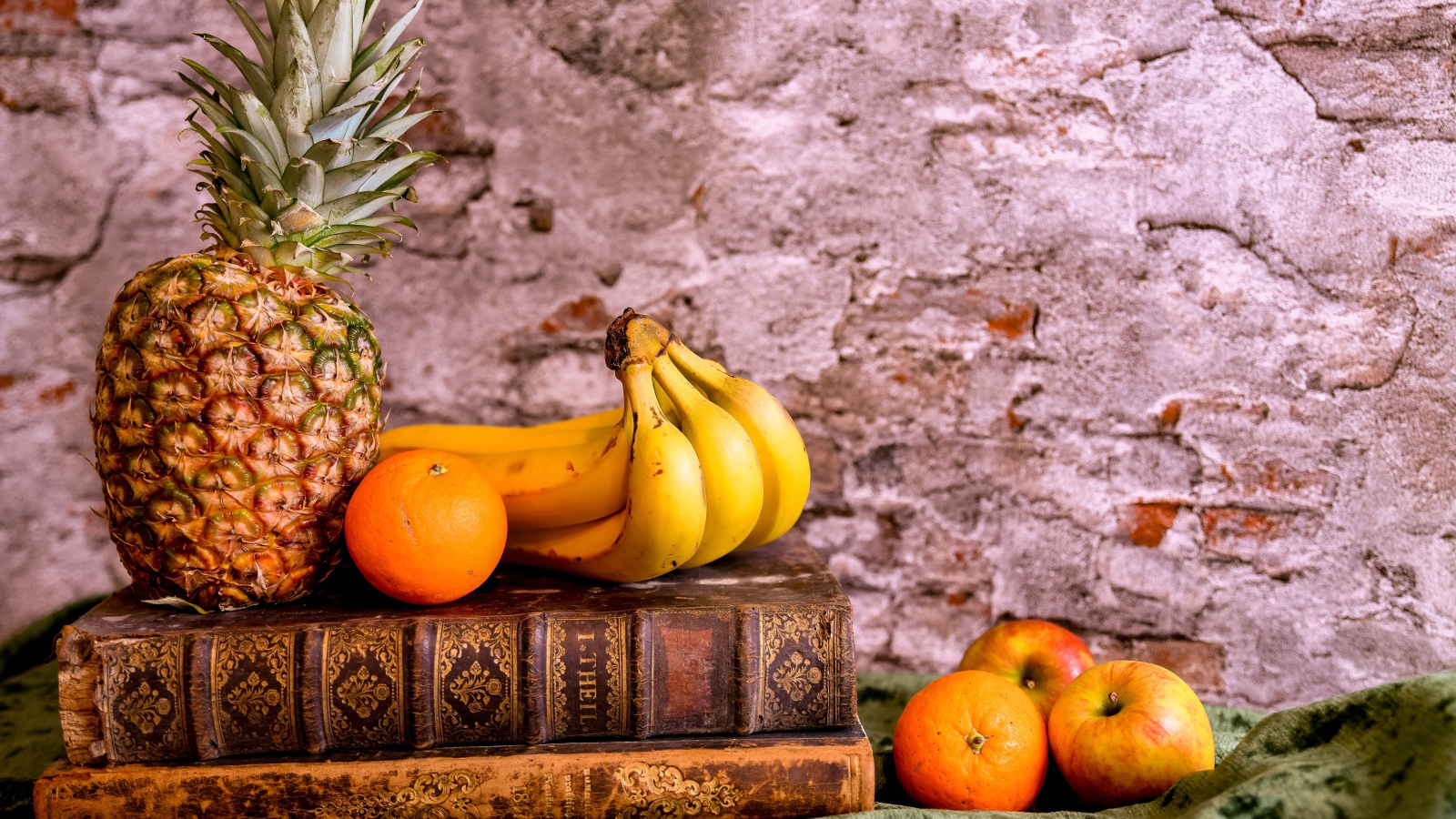 Апельсины, бананы, яблоки и ананас на столе со старыми книгами