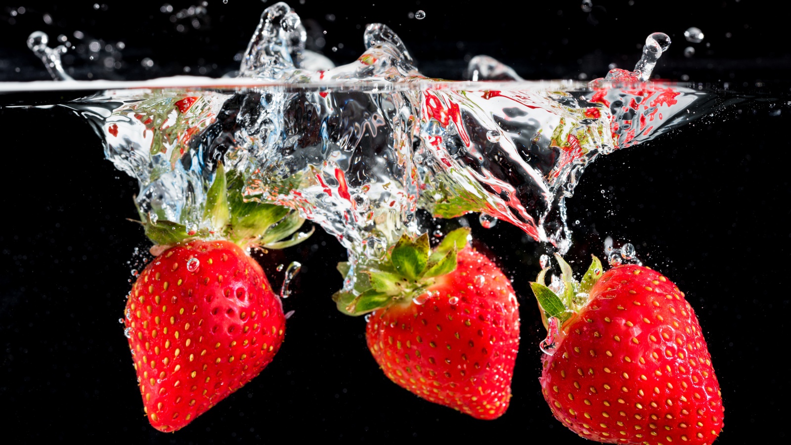 Три ягоды клубники в воде на черном фоне