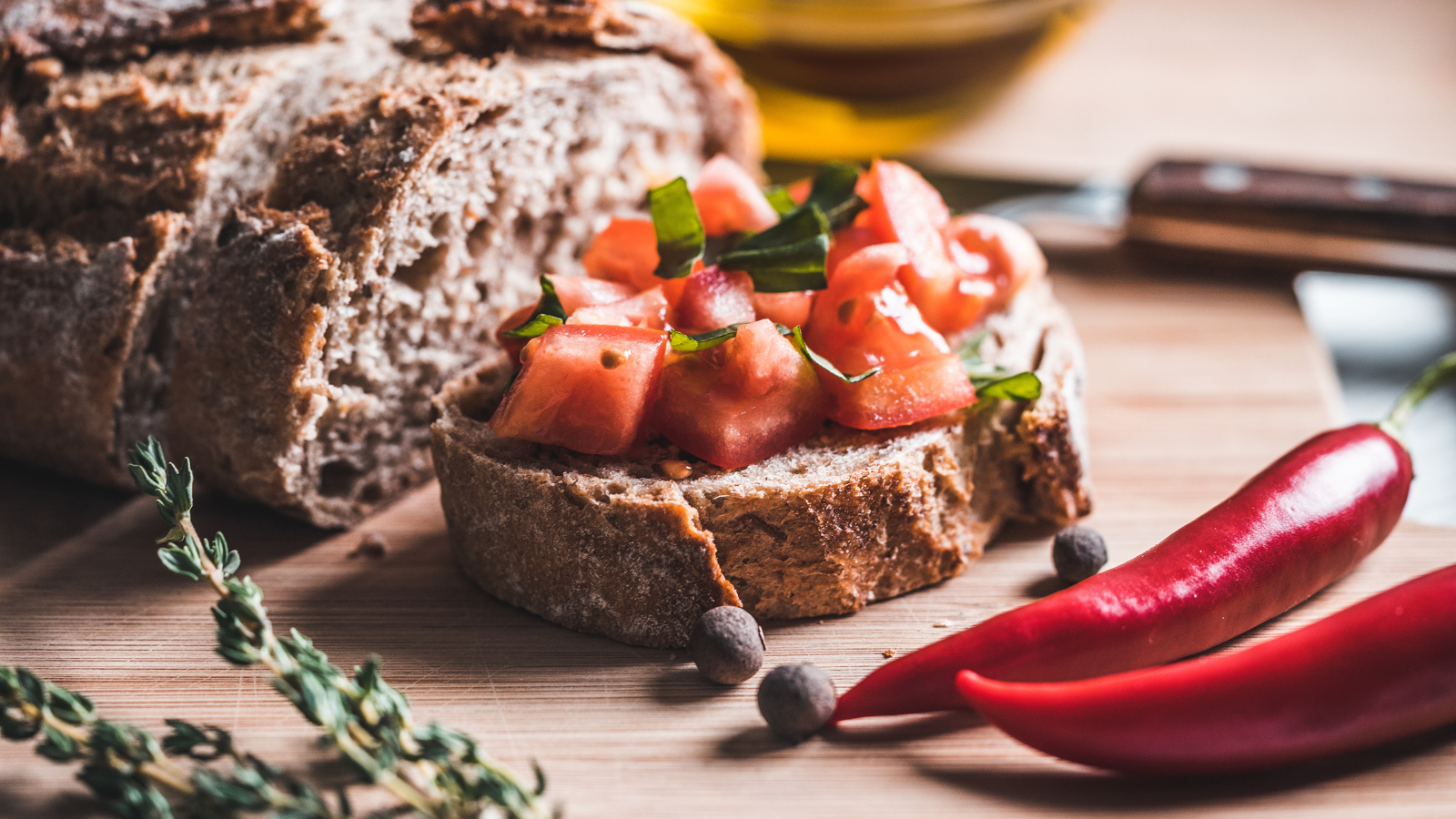 Черный хлеб с кусочками помидора на столе с острым красным перцем