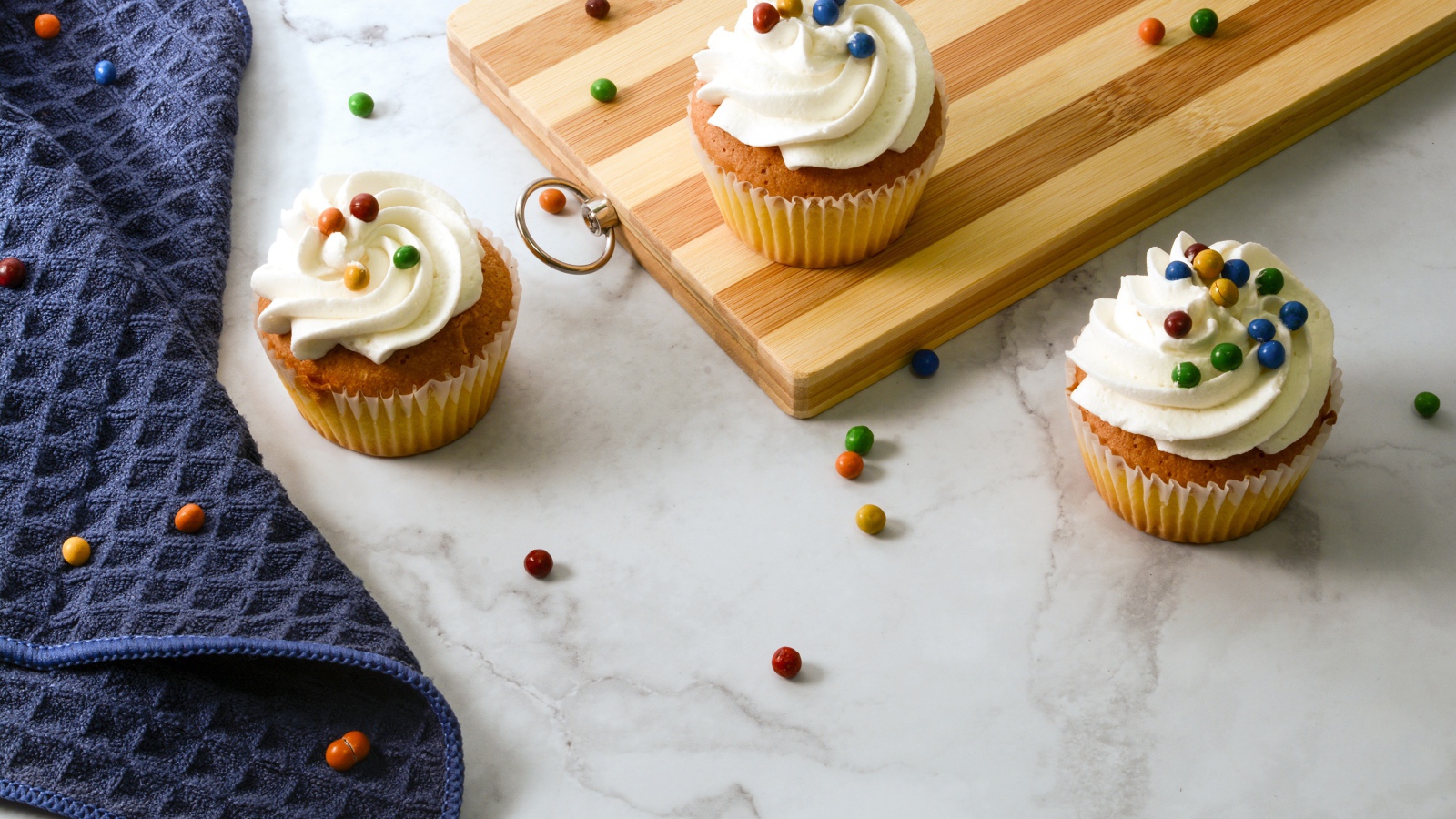 Кексы с кремом и разноцветными шариками на столе с доской