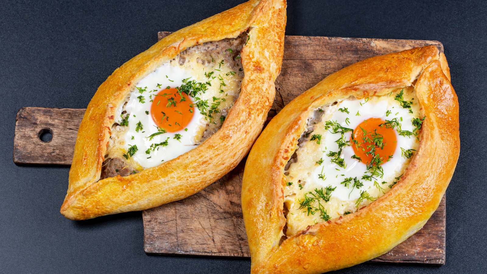 Два больших свежих хачапури с яйцом на доске