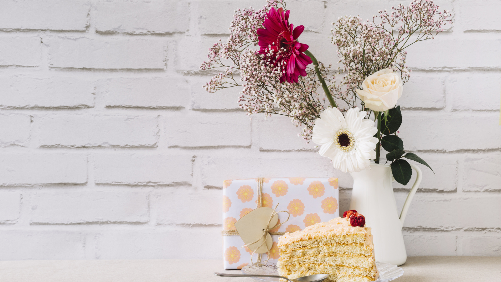 Кусок торта, подарок и букет на столе на фоне стены 