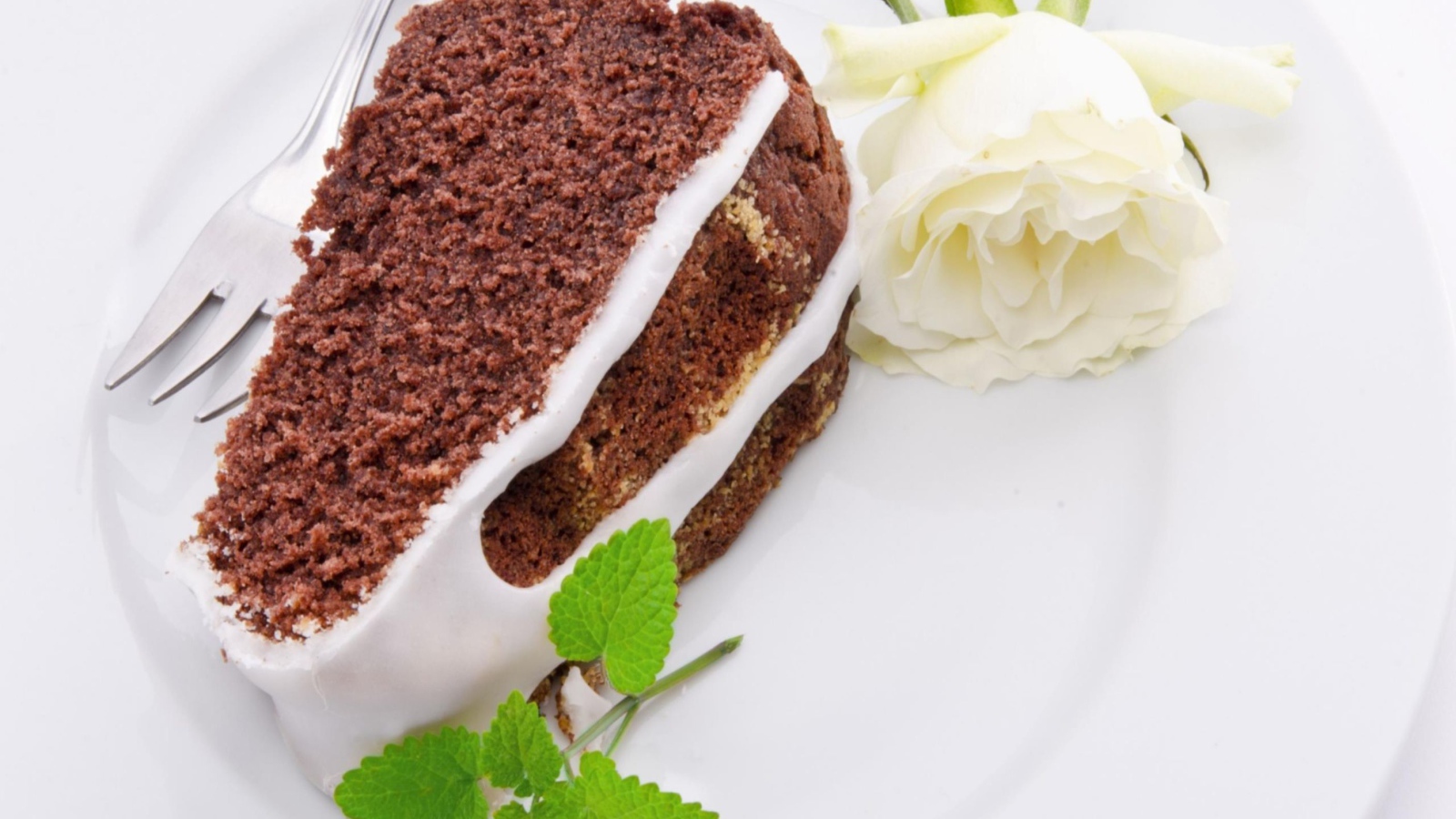 Кусок шоколадного пирога на тарелке с белой розой 