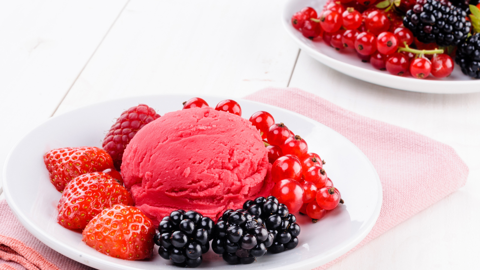 Шарик фруктового мороженого с ягодами на белой тарелке