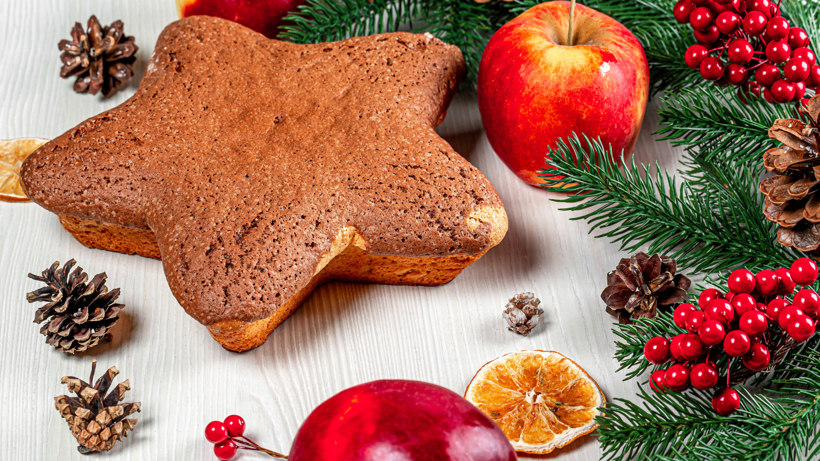 Рождественский кекс на столе с еловыми ветками,  яблоками и шишками