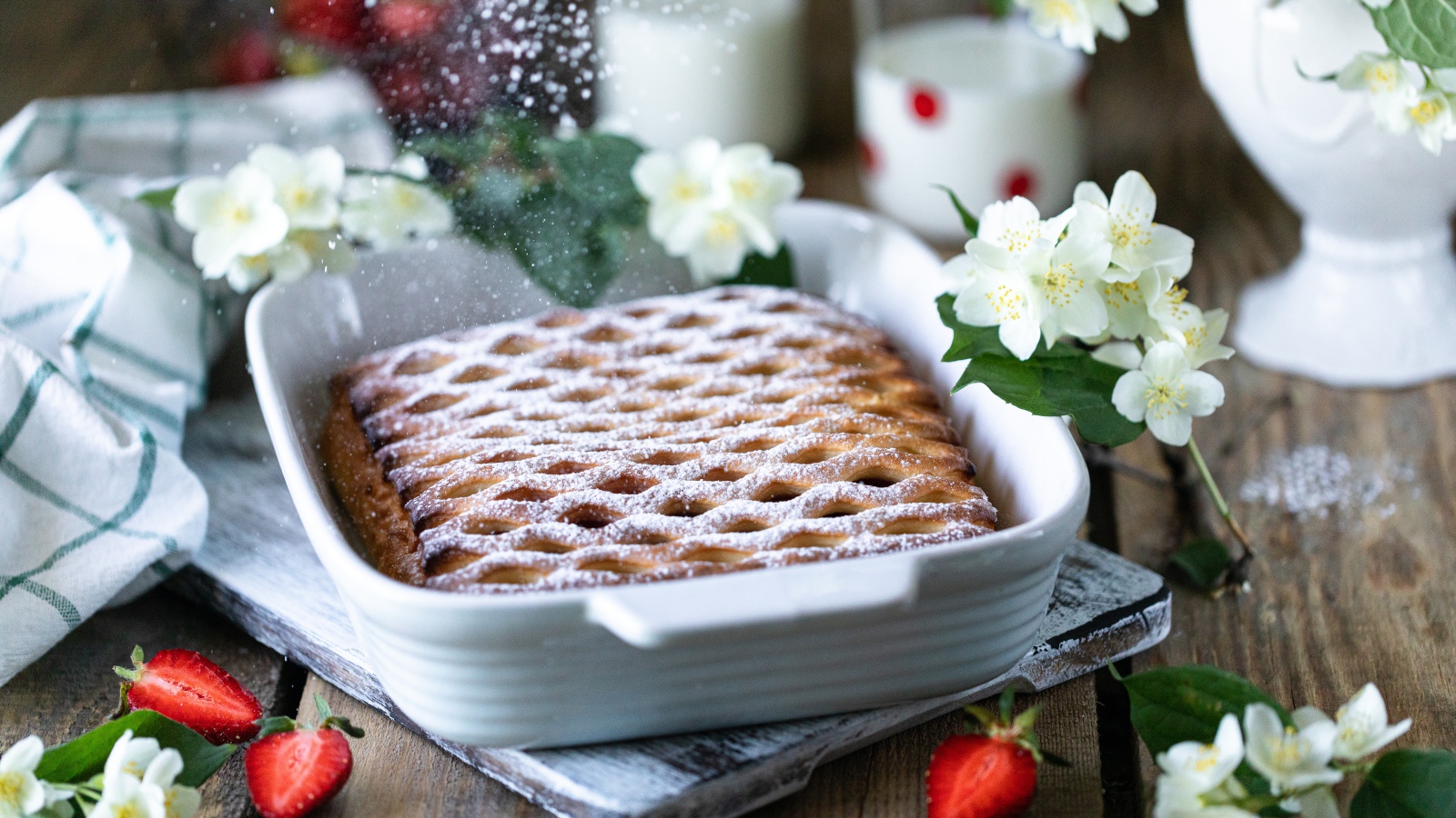 Вкусный клубничный пирог с сахарной пудрой на столе с цветами жасмина