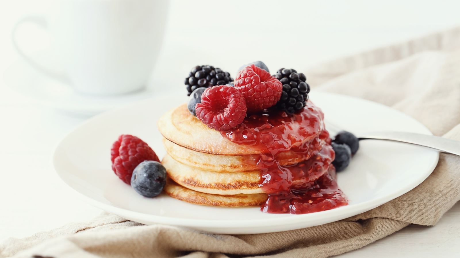 Оладьи на большой белой тарелке с джемом и ягодами 