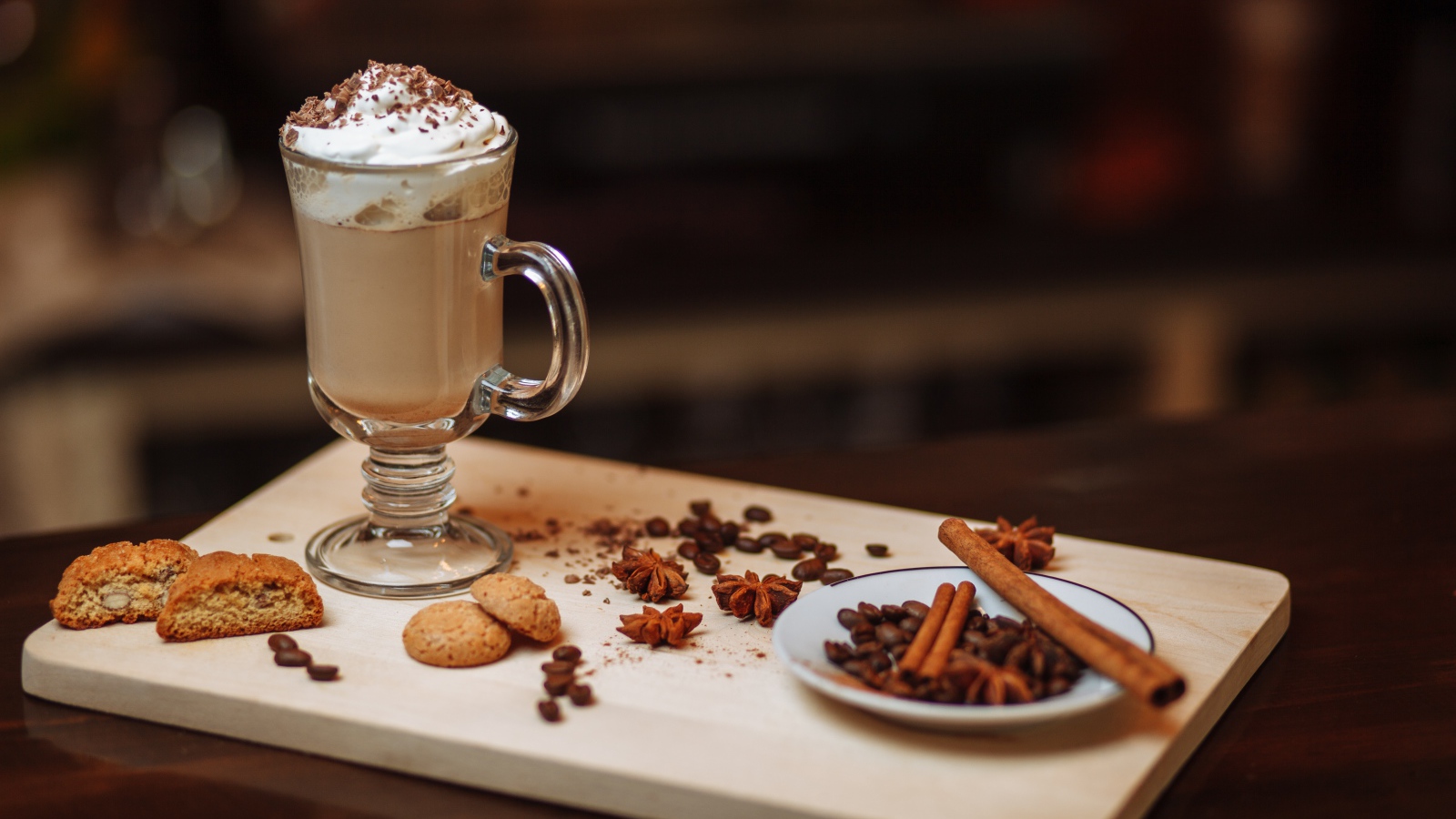 Горячее какао со сливками на столе с печеньем, зернами кофе и пряностями 