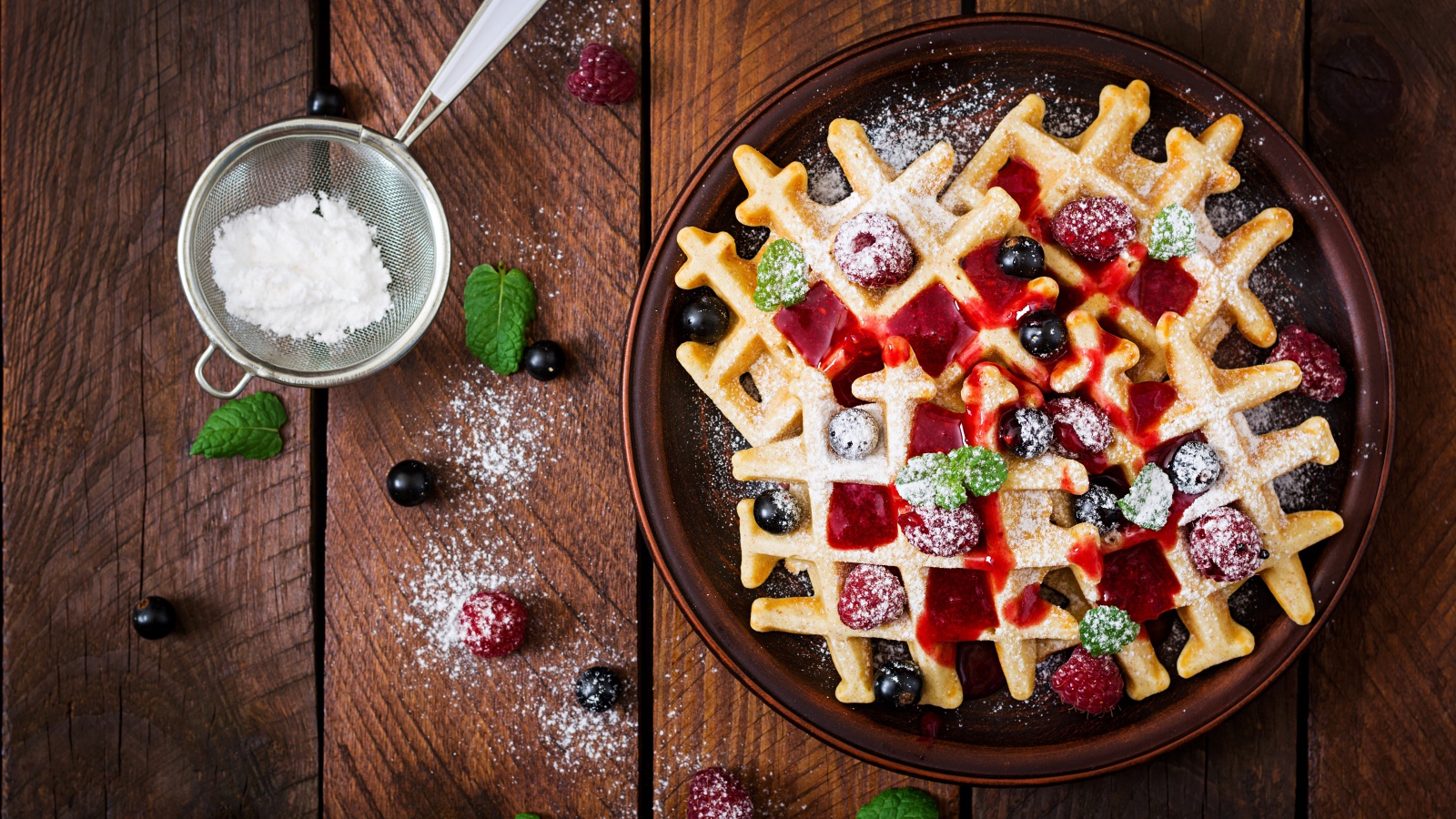 Сладкие медовые вафли на тарелке с ягодами и джемом и сахарной пудрой 