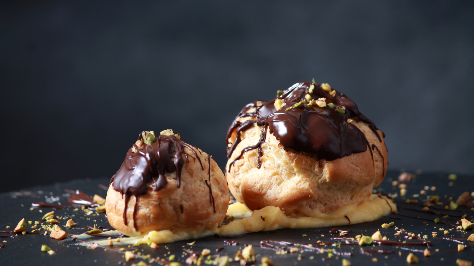 Два заварных пирожных с шоколадом на сером фоне