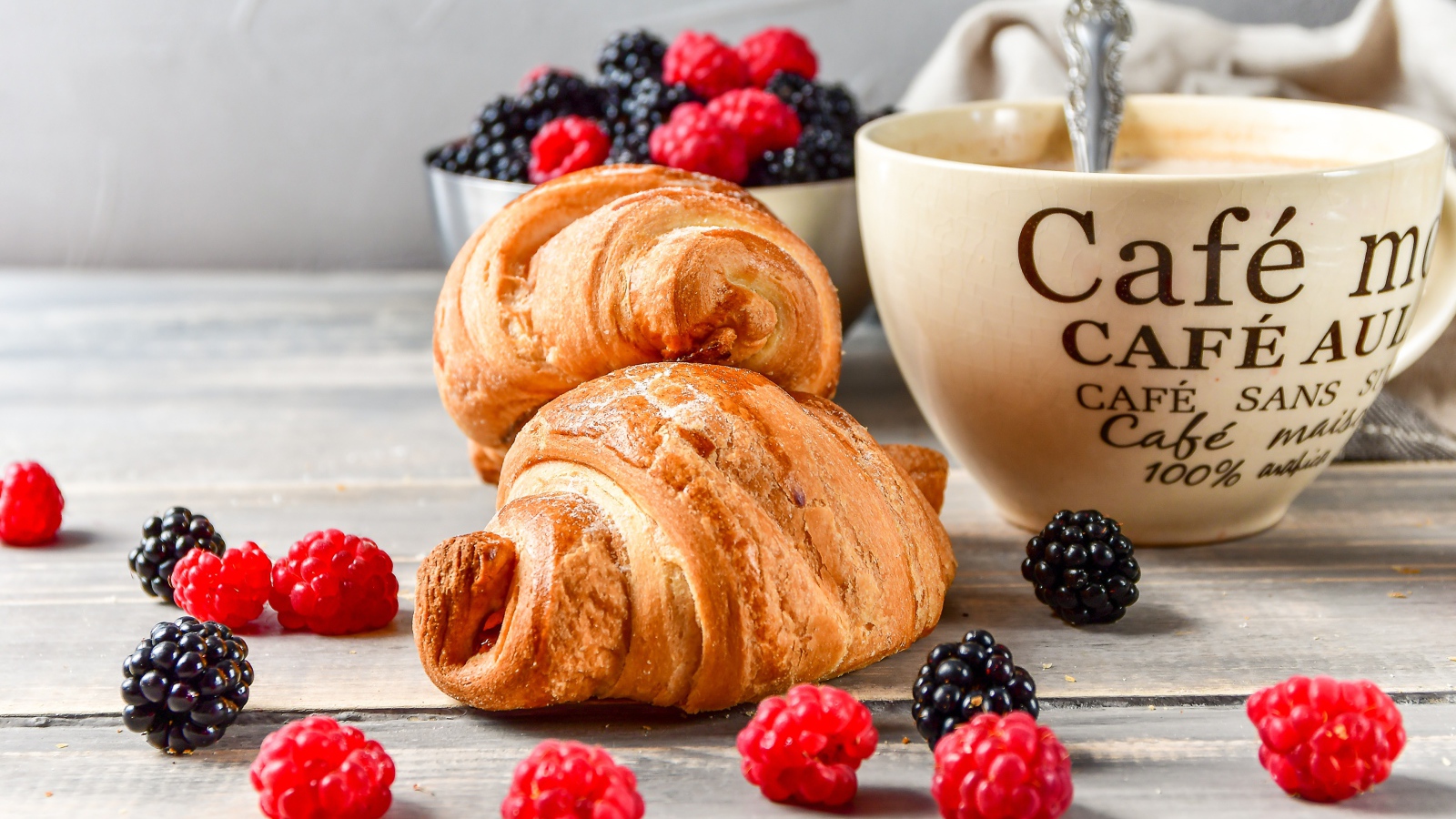 Два круассана на столе с чашкой кофе и ягодами