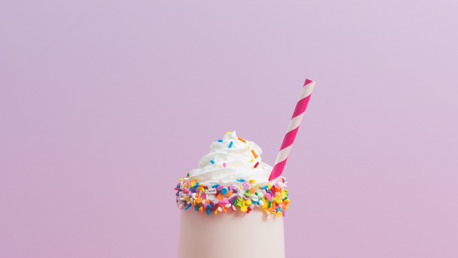 Коктейль  в стакане со взбитыми сливками на розовом фоне