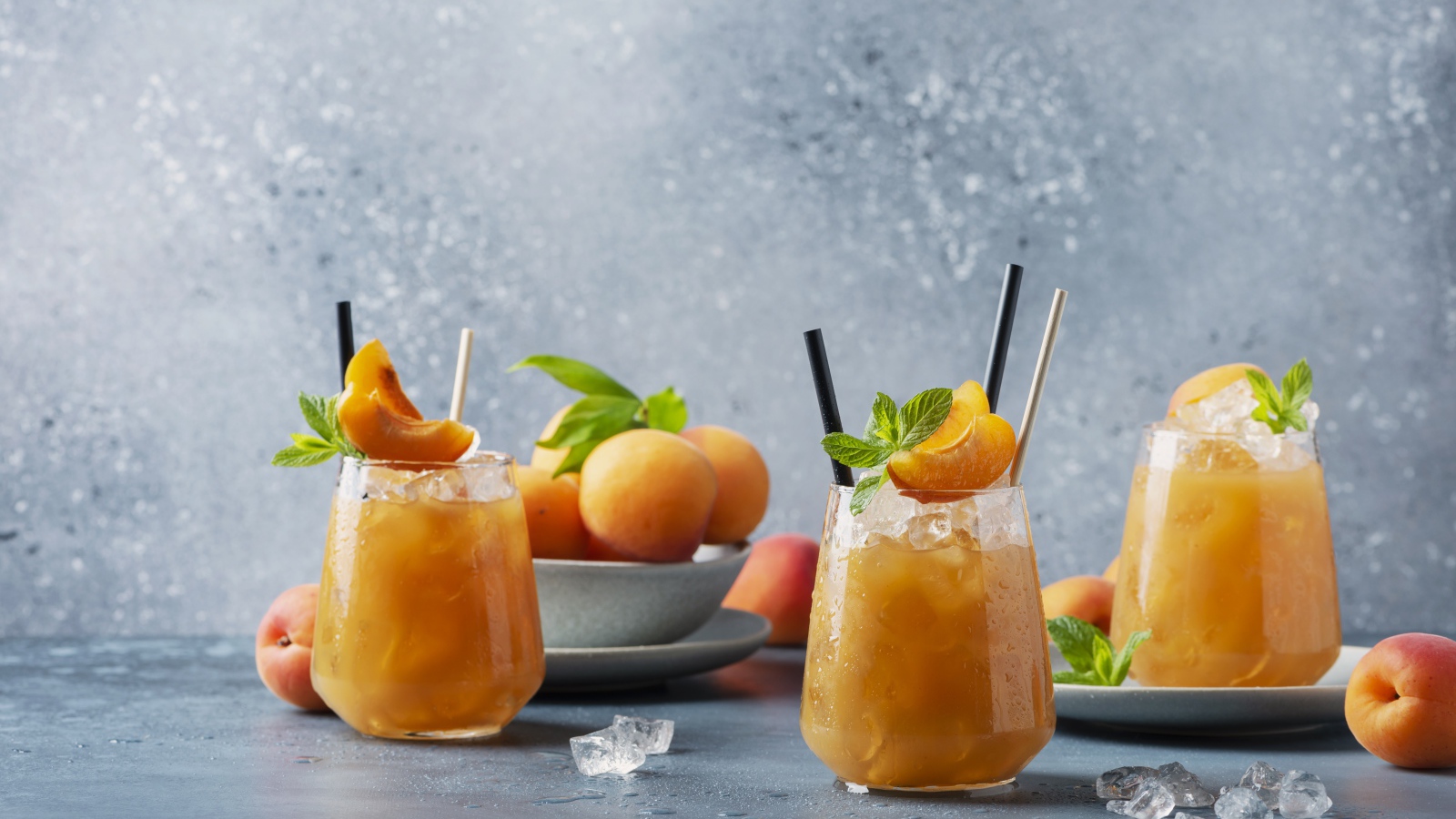 Холодный абрикосовый напиток со льдом в стаканах на столе со свежими абрикосами