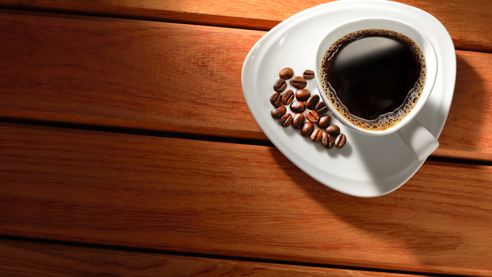 Чашка кофе на тарелке с зернами на деревянном столе