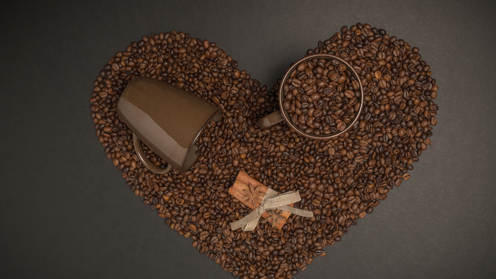 Сердце из кофейных зерен на сером фоне с кружками 