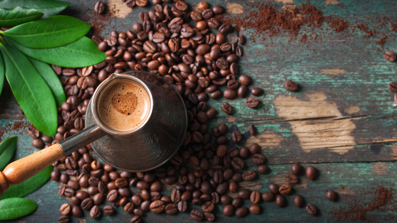 Турка с кофе на столе с зернами и зелеными листьями