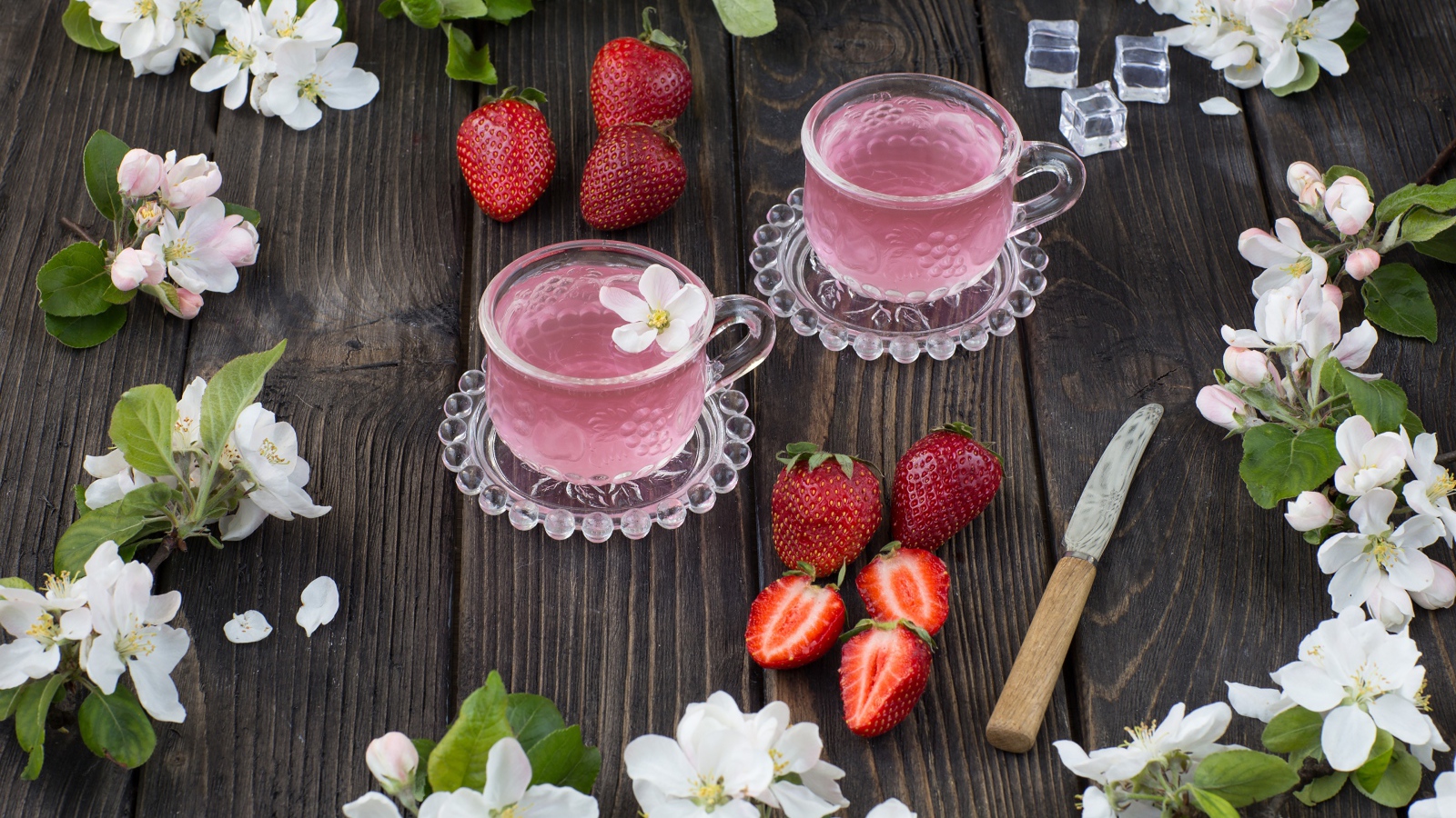 Две стеклянные чашки ягодного чая на столе с клубникой и цветами яблони