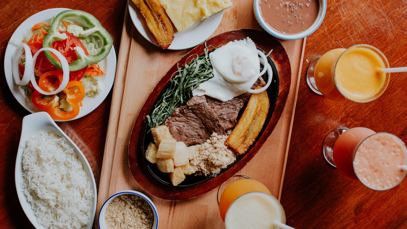 Кусок мяса в жаровне на столе с напитками, овощами и рисом