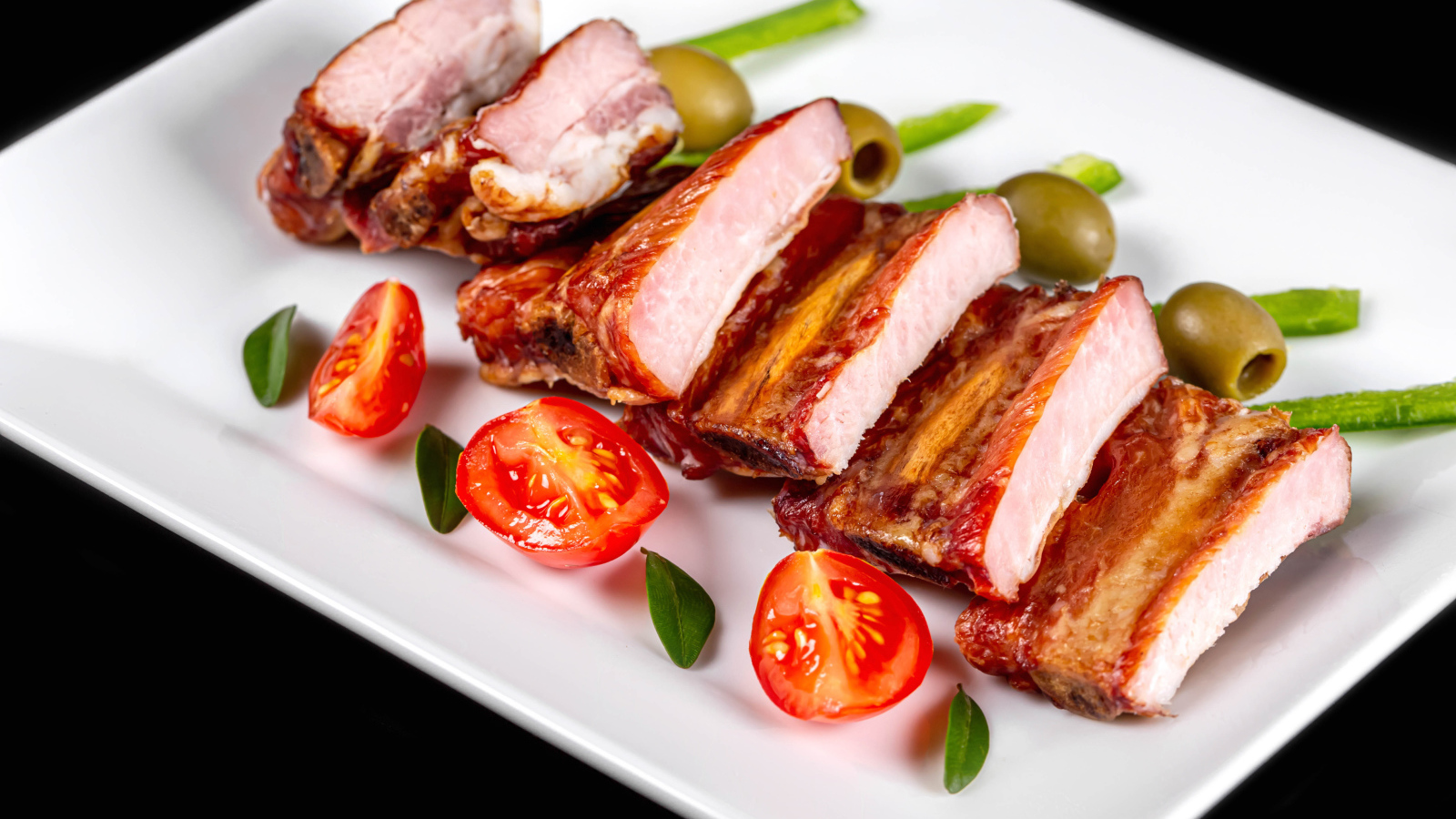 Запеченные ребрышки на белой тарелке с помидорами и оливками