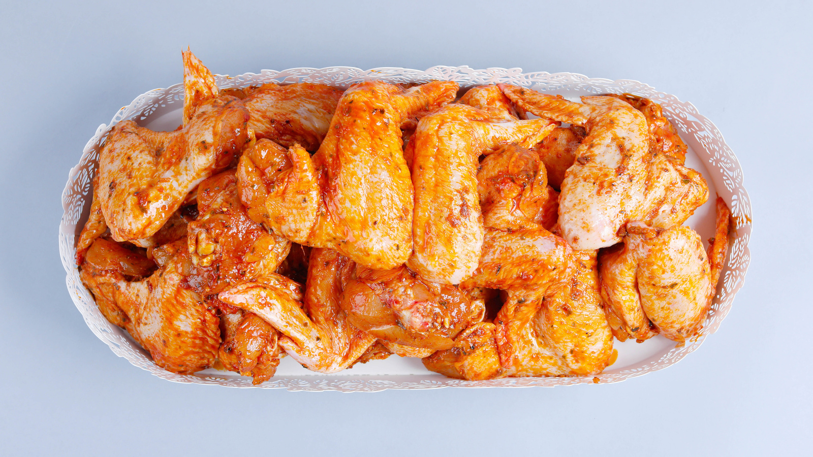 Жареные куриные крылья в белой корзине на сером фоне